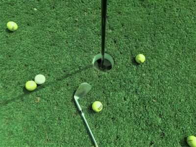 Bild auf dem ein Golfplatz mit dem Hole, einem Schläger, vielen Golfbällen abgebildet ist